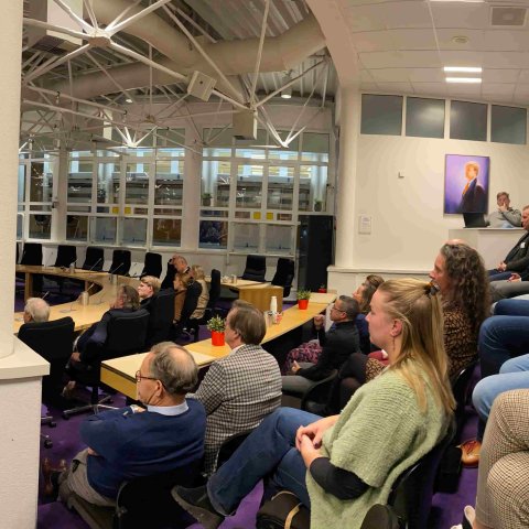 Foto van de aanwezigen in de raadzaal van het gemeentehuis die luisteren naar de spreker.
