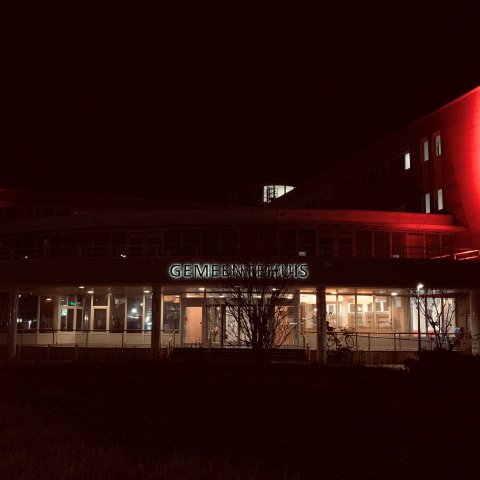 De voorkant van het gemeentehuis van Huizen in het donker, met oranje verlichting.