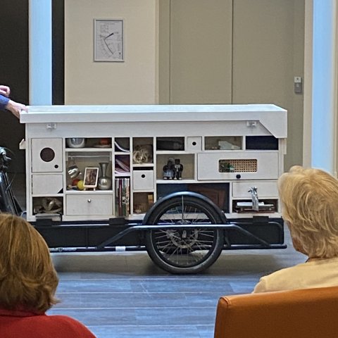 Fietsaanhanger dat lijkt op een soort kast met verschillende spullen zoals boeken, beeldjes, fotolijst, enzovoort