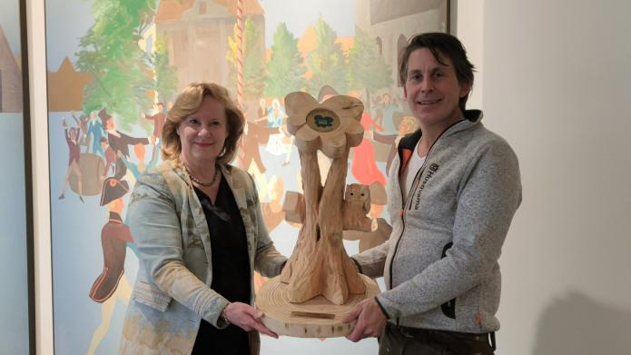 Wethouder Verbeek neemt een houten kunstwerk in ontvangst uit handen van meneer Hoekstra