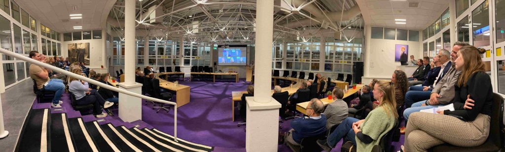 Foto van de aanwezigen in de raadzaal van het gemeentehuis die luisteren naar de spreker.