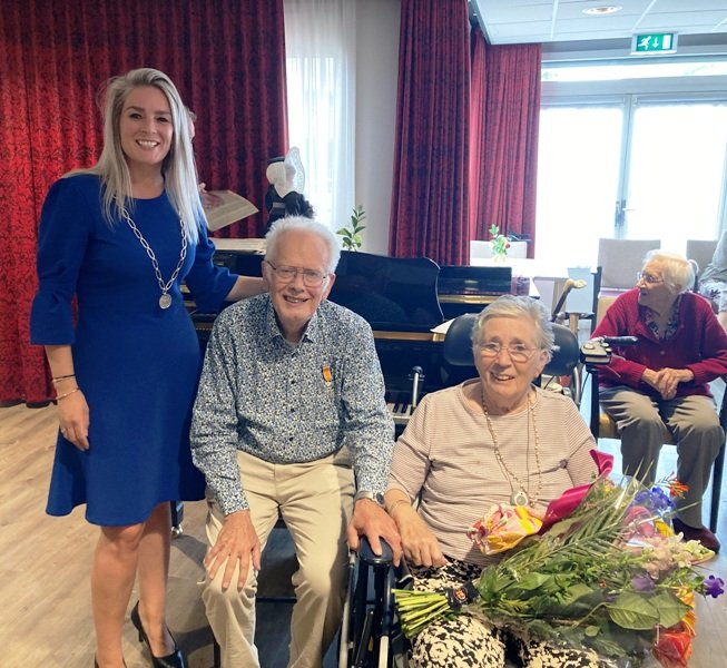 Wethouder Fleur van der Kleij, samen met decorandus Jan Vlek en naast hem zijn vrouw met een bos bloemen in de hand.