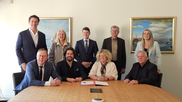 De collegeleden en andere betrokken personen zitten aan een vergadertafel met daarop een ondertekend document