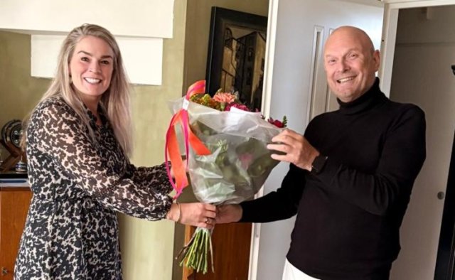 Wethouder Fleur van der Kleij kijkt lachend naar de camera en overhandigt Roelof de Kroes een bosje bloemen.