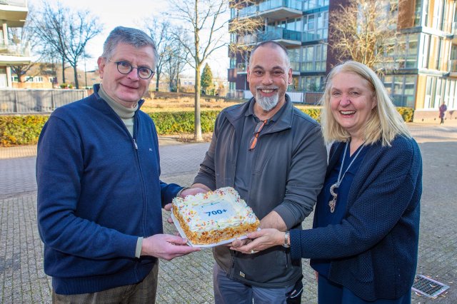 Wethouders Bert Rebel (Duurzaamheid) en Karin van Werven (Armoedebeleid) geven taart aan hoofdfixer Eddy Stecher van de Fixbrigade. Op de traat staat '700+'.