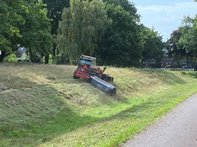 Tractor staat schuin op een berm en maait daar het gras