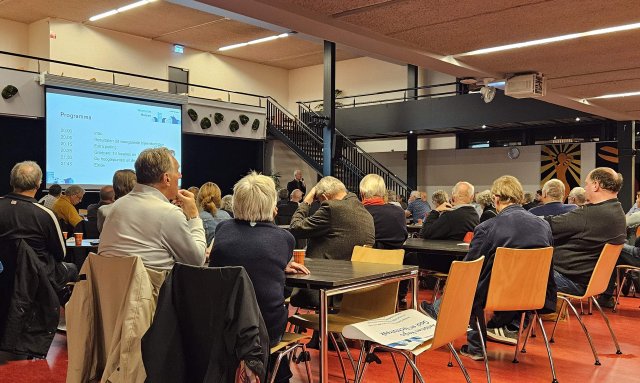 Groep zittende mensen in een ruimte met een groot presentatiescherm