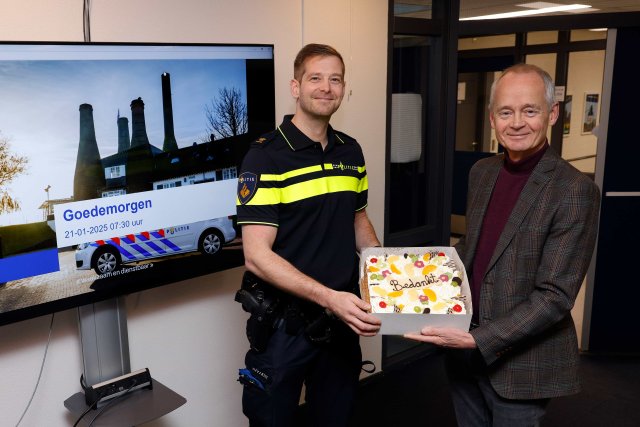 Een tevreden kijkende burgemeester overhandigt de teamchef van de politie een taart, met daarop de tekst: Bedankt.