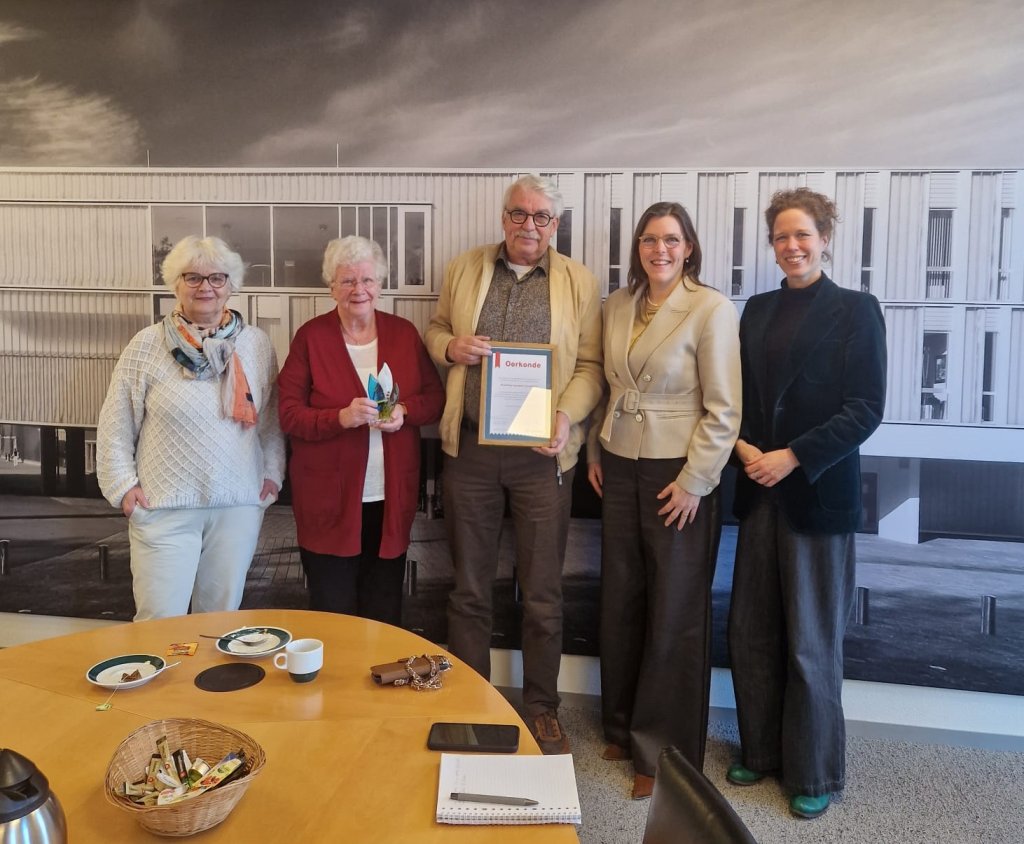 Leden van het bestuur van Stichting Leergeld poseren met het ontvangen Compliment naast wethouder Eveline Schell en burgemeester Ester Weststeijn