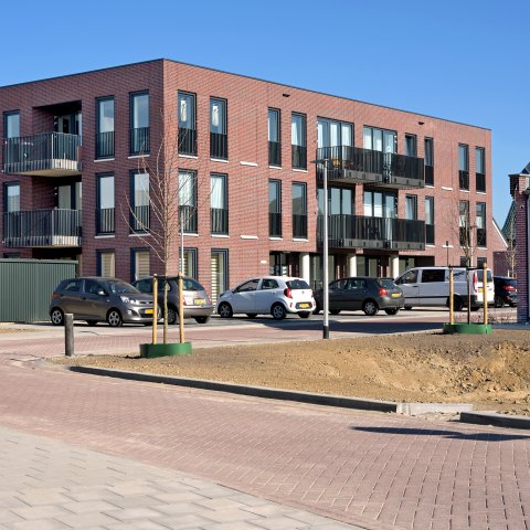 Appartementengebouw van drie etages met balkons. Geparkeerde auto's.