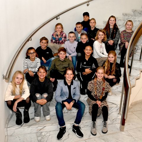 Members of the children's council sit on the marble steps of the town hall and smile into the camera