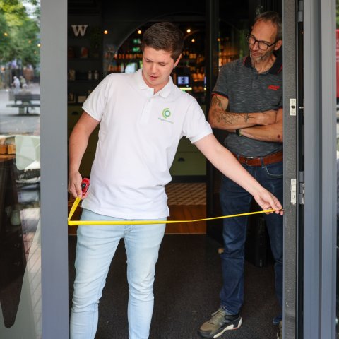 Iemand van de werkgroep Ongehinderd meet de breedte van een deur op