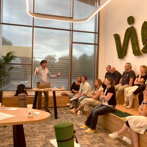 Een groep mensen luistert naar een persoon die een presentatie geeft in Vie