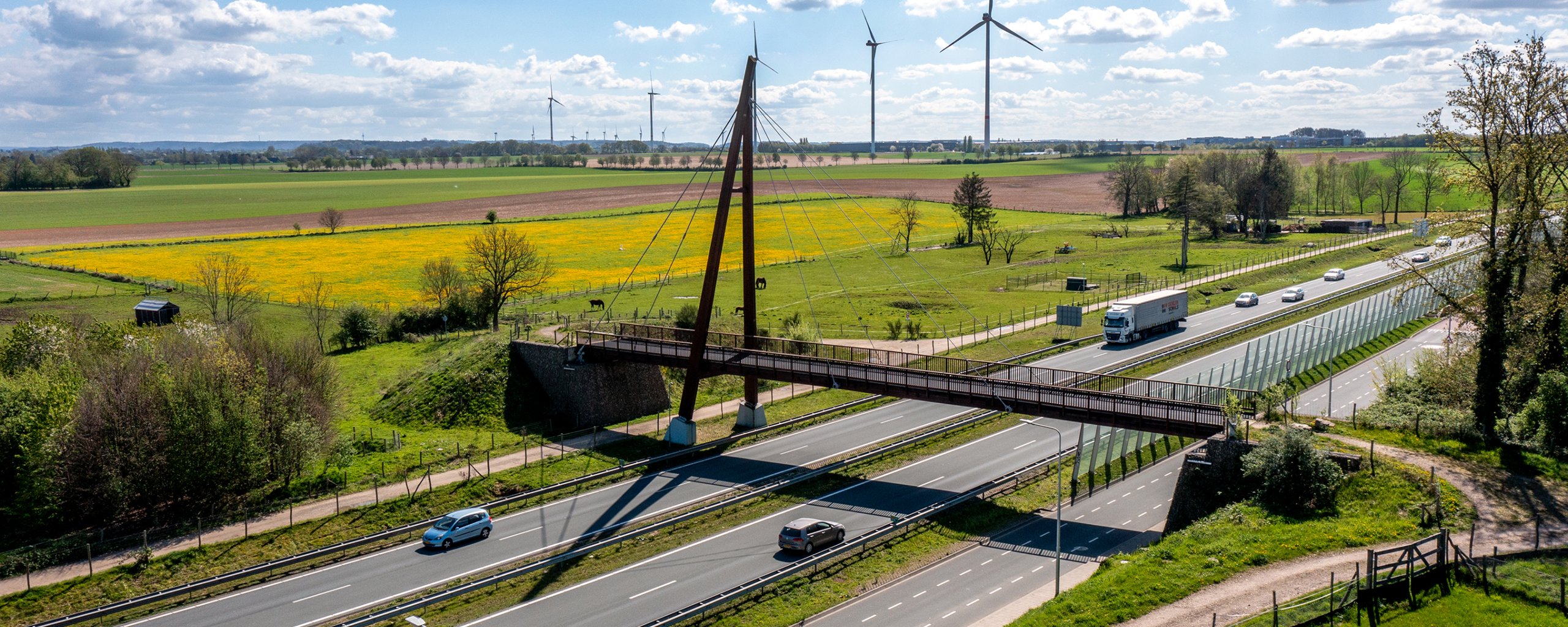 De brug over de Hamweg en de Buitenring. Op de voorgrond een wandelpad, op de achtergrond velden en windmolens. 