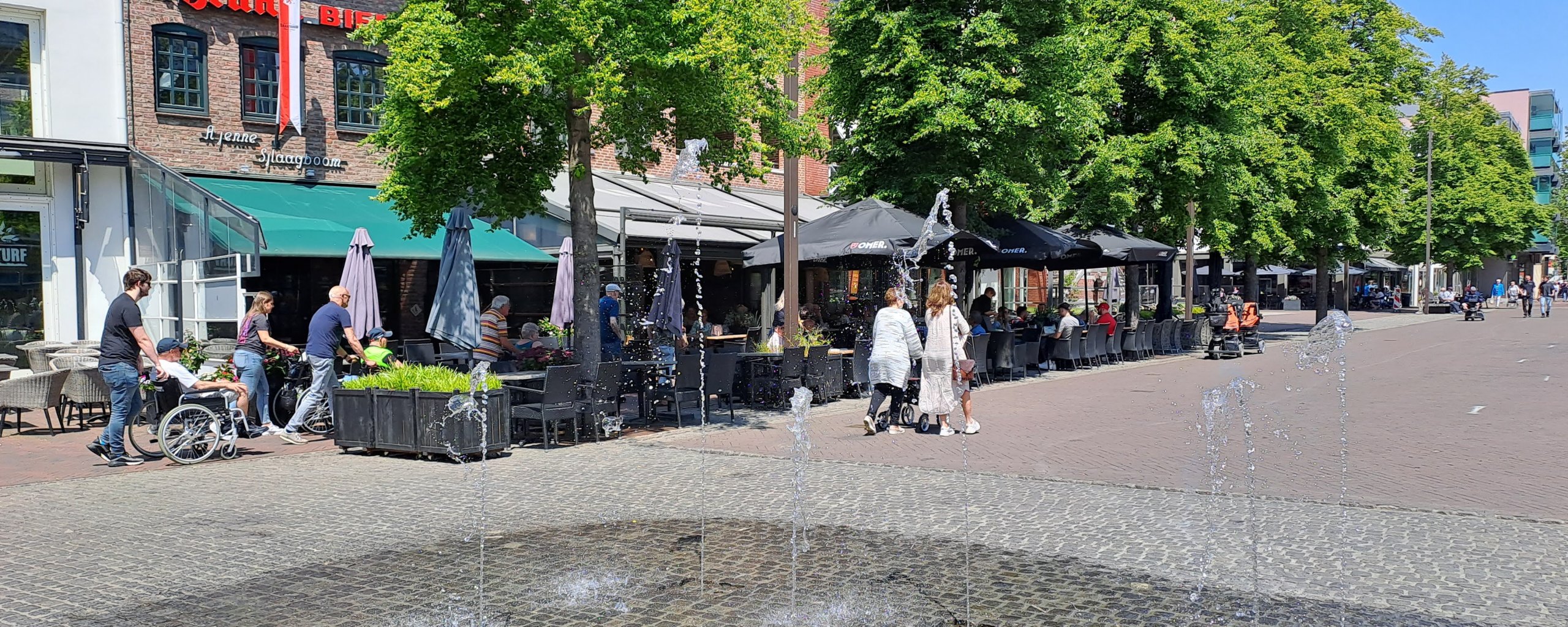 Een zomerse foto van de horeca aan de Markt. Op de voorgrond de fonteintjes. Op de achtergrond lopen mensne langs