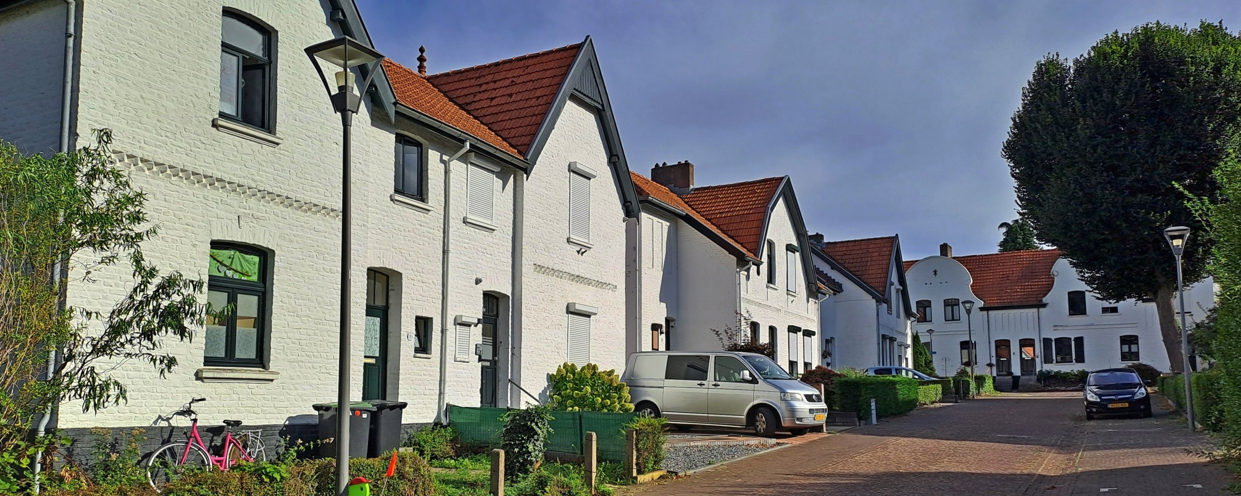 A street with white houses on the left. Parked cars.