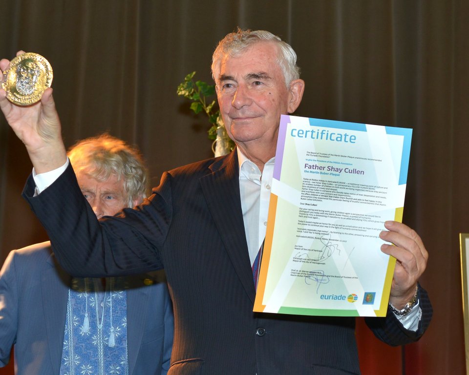 Father Shay Cullen holds up the Buber plaque in one hand and the certificate in his other hand