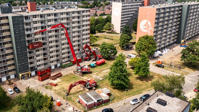 Een dronefoto van de flat aan de Hertogenlaan in Rolduckerveld. Het is duidelijk te zien dat de voorbereidingen voor de sloop getroffen worden: er staan verschillende hoogwerkers en graafmachines.