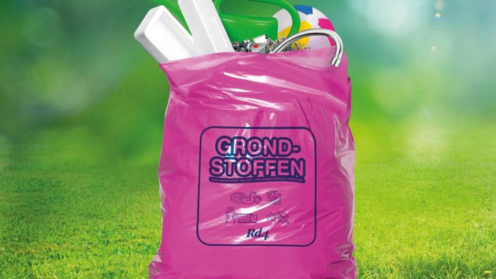 Een roze tas met daarin afval. De tas staat in het gras