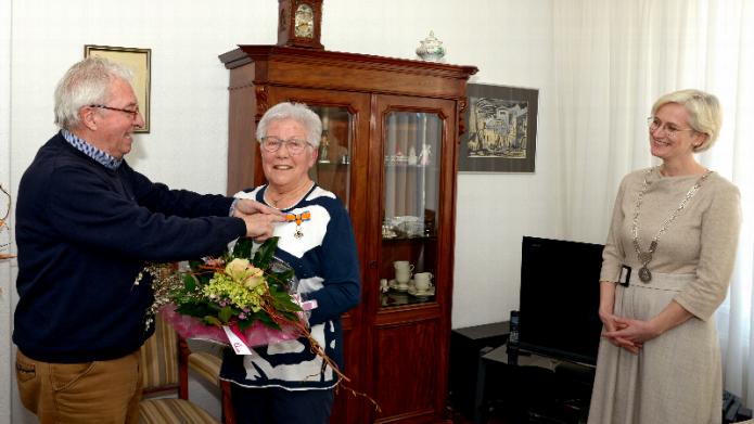 Haar man Jan speldt de onderscheiding op bij mevrouw Savelkoul, burgemeester Dassen kijkt op afstand toe