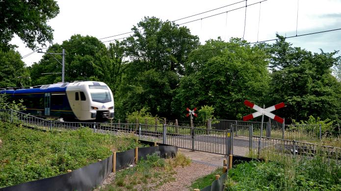 Een onbewaakte spoorwegovergang waar een trein passeert. De toegang tot de overweg is afgesloten met hekken. 