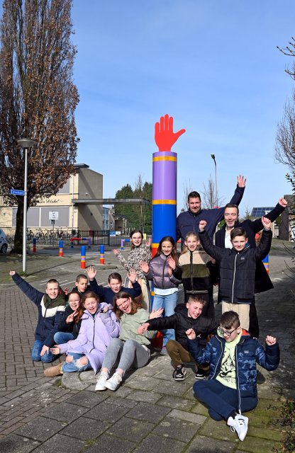 Wethouder Geers en een groep kinderen bij een gekleurde paal met een rood handje erop. Ze juichen allemaal. 