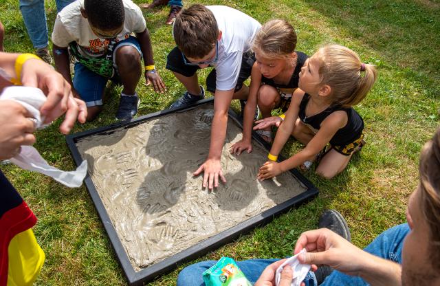 Een aantal kinderen laat een handafdruk achter in beton. De plaat met beton ligt op het gras.