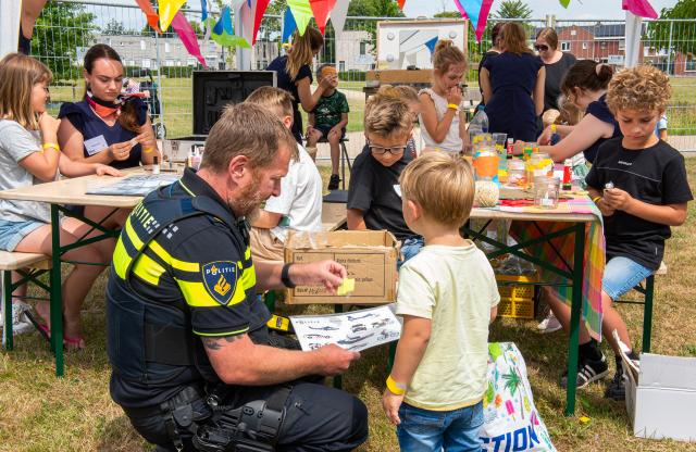 Een politieagent in uniform helpt een kindje bij het uitzoeken van een glittertattoo bij een kraampje