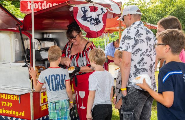 Een aantal kinderen en een volwassene staan in de rij voor een rode hotdogkraam. 