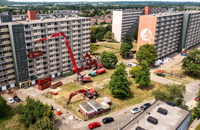 Een dronefoto van de flat aan de Hertogenlaan in Rolduckerveld. Het is duidelijk te zien dat de voorbereidingen voor de sloop getroffen worden: er staan verschillende hoogwerkers en graafmachines.