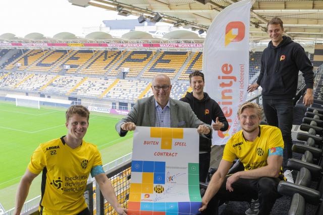 Wethouder Schlangen en de verschillende partners laten het buitenspeelcontract zien. Ze zitten op de tribune van het Parkstad Limburg Stadion.