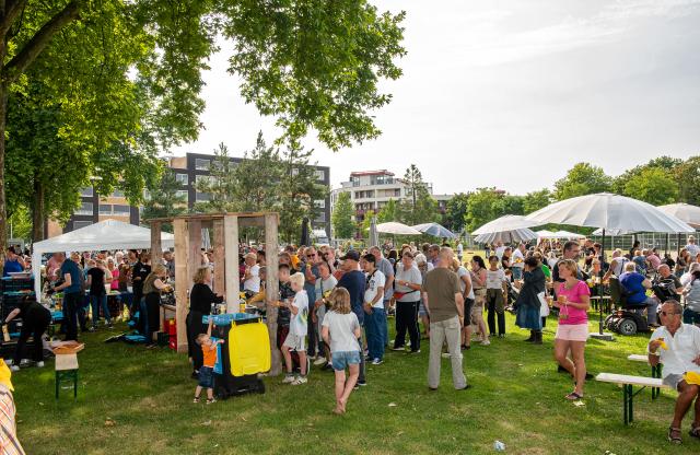 Bezoekers van festival Thuis in West staan gezellig bij elkaar, er staan partytenten en parasols tegen de zon. 