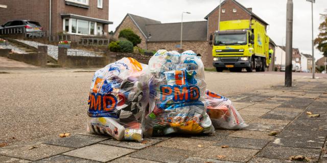 Op de voorgrond enkele PMD zakken buiten op de stoep, op de achtergrond de Rd4-wagen die ze komt ophalen