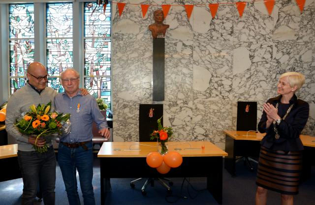 De heer Van Veen en zijn zoon poseren voor de camera, burgemeester Dassen applaudisseert op afstand