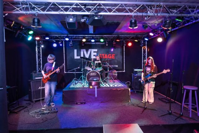 Een band op een podium; een gitarist, bassist en drummer.