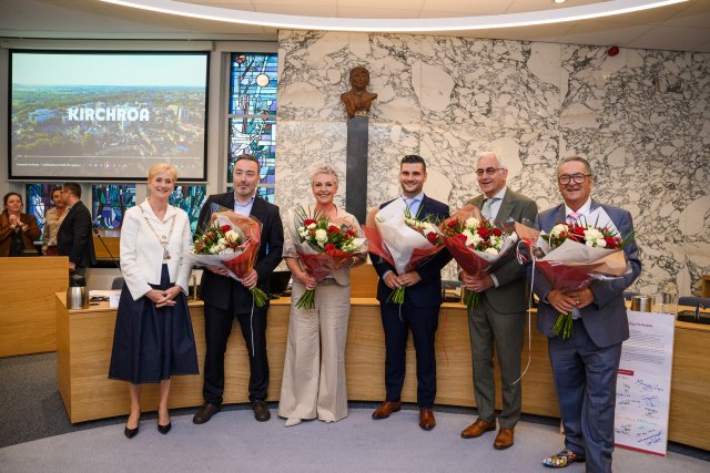 De burgemeester staat naast de wethouders die net zijn beëdigd en allemaal een bos bloemen in hun handen hebben