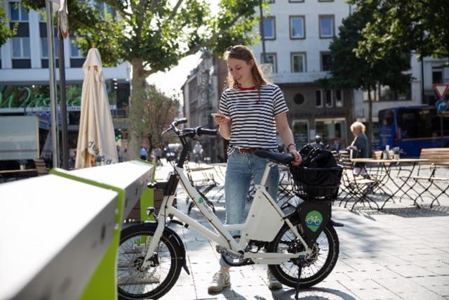 Een mevrouw parkeert haar elektrische fiets bij een laadstation. 