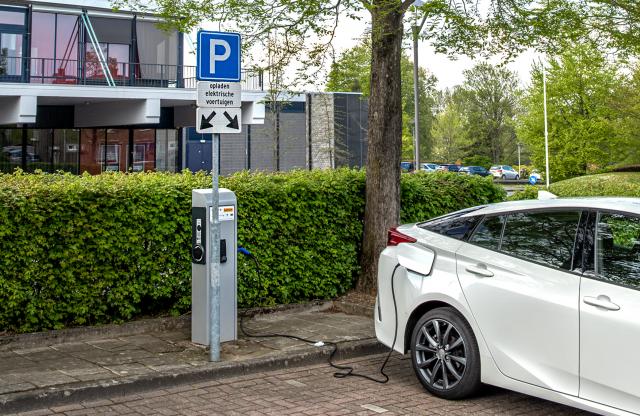 Een laadpaal bij een parkeervak voor electrische auto's. Er loopt een kabel naar een witte auto. 