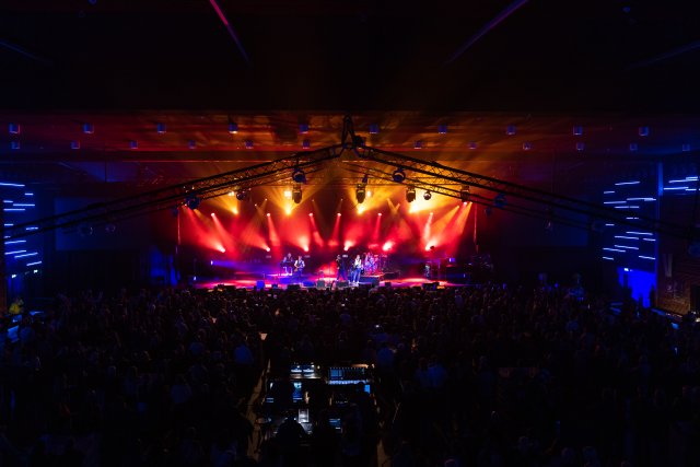 Een optreden voor een volle zaal in de Rodahal. Het podium is paars-rood-gele verlicht