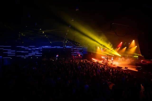 Een optreden voor een volle zaal in de Rodahal. Het podium is oranje-gele verlicht