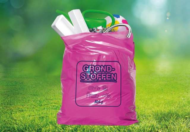 Een roze tas met daarin afval. De tas staat in het gras