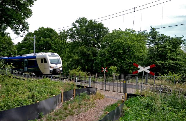 Een onbewaakte spoorwegovergang waar een trein passeert. De toegang tot de overweg is afgesloten met hekken. 