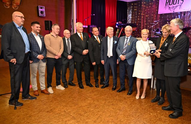 Burgemeester Dassen reikt de erepenning uit terwijl een groep mensen toekijkt