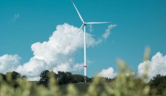 Een witte windmolen op een groene heuvel met blauwe lucht en enkele witte wolken