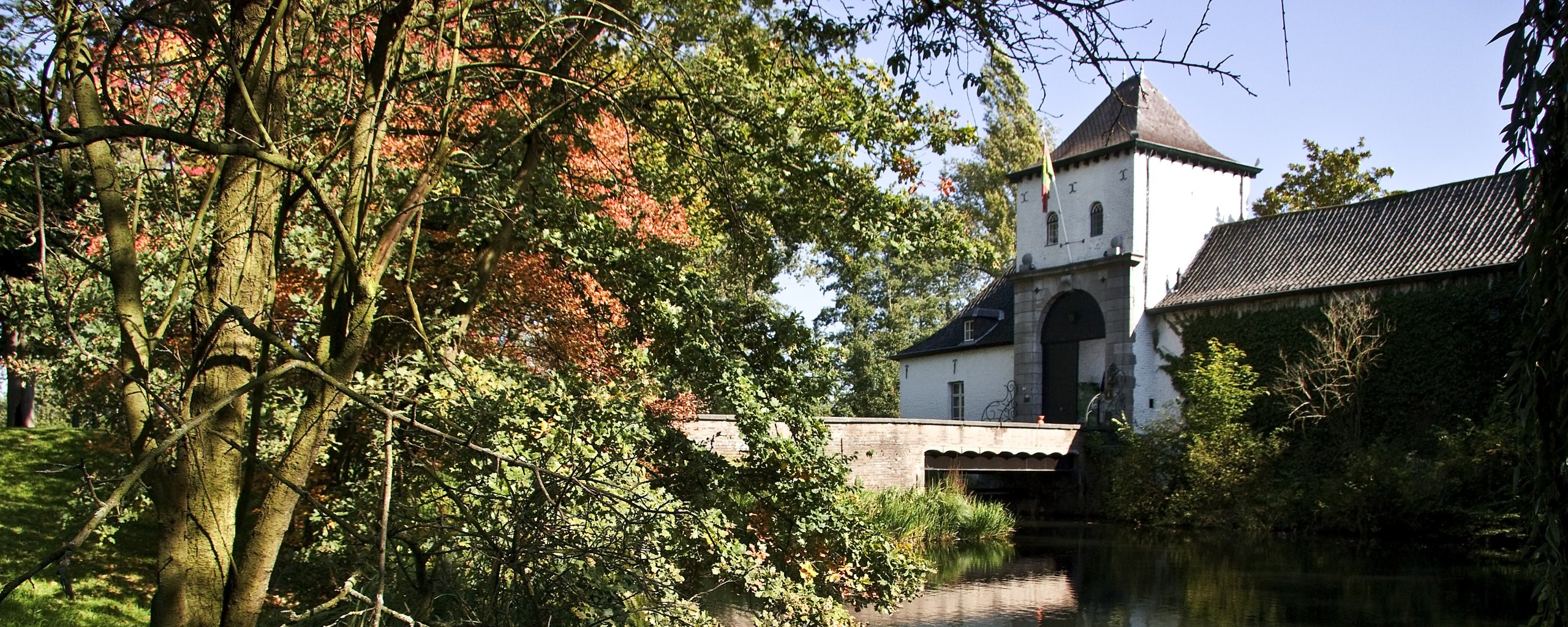 Bomen en water met rechts de brug en de entree van kasteel Daelenbroeck in Herkenbosch