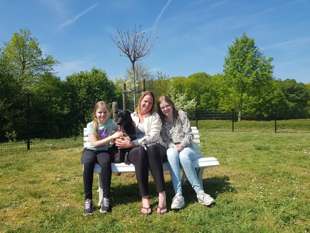 We zien drie vrouwen op een bankje in een omheind veld. Het zijn de initiatiefnemers van het hondenspeelveld in Herkenbosch. Hun hond is ook zichtbaar op de foto.