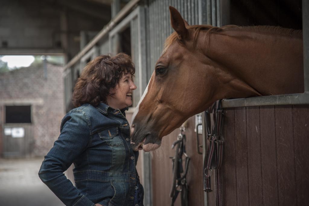 Een vrouw staat voor een paard in een stal.