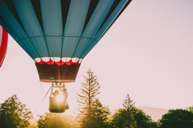 Het onderste deel van een blauwe luchtballon, de mand onder de ballon en op de achtergrond een zonsondergang.