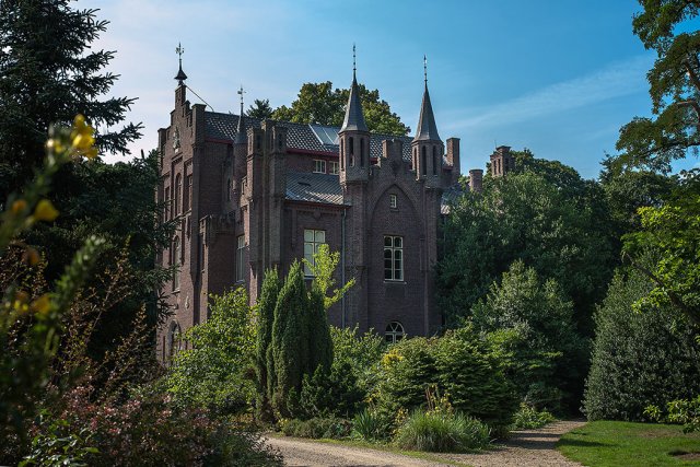 Een kasteel met twee spitse torens ten midden van groene bomen.