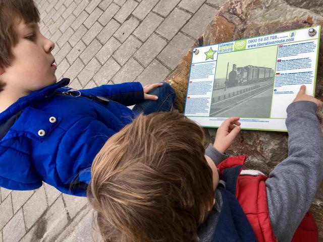 Twee kinderen die naar een bordje kijken met informatie over een trein uit de tweede wereldoorlog. Het bordje is onderdeel van de Liberation Route.